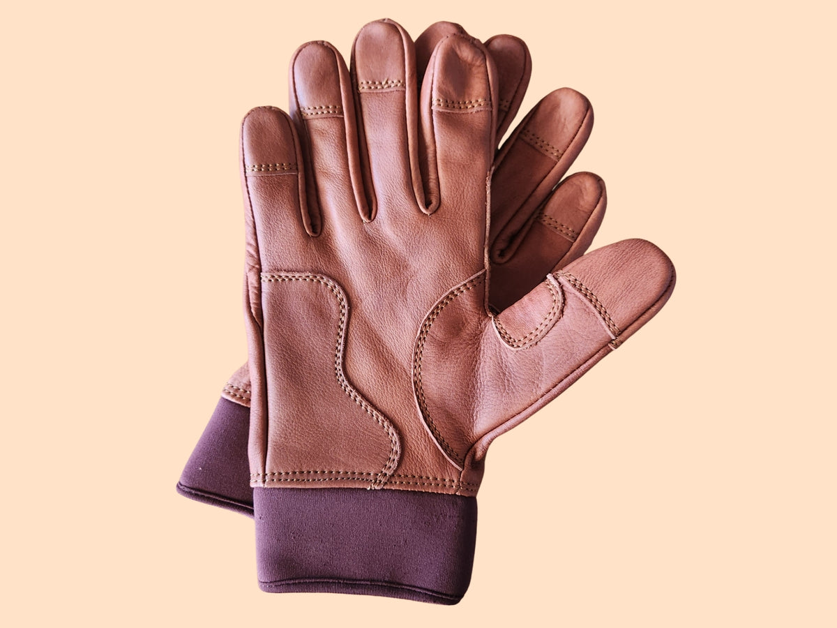 A pair of brown leather gloves with a contrasting dark purple knit cuff, displayed against a solid pale peach background.